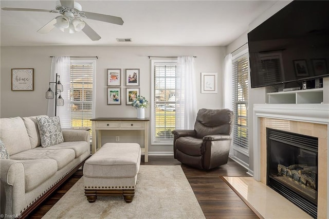 living room with visible vents, dark wood-style floors, baseboards, ceiling fan, and a tile fireplace