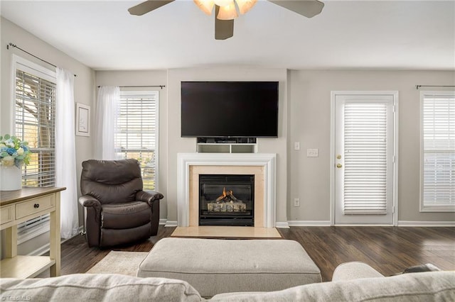 living area featuring a premium fireplace, baseboards, a ceiling fan, and wood finished floors