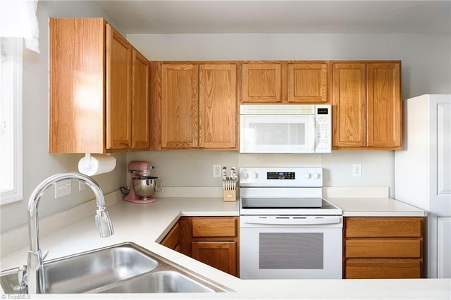 kitchen with white appliances, brown cabinetry, light countertops, and a sink