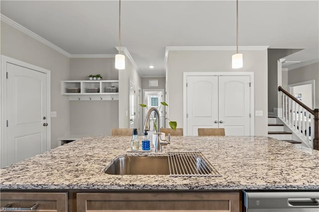 kitchen featuring sink, ornamental molding, hanging light fixtures, and an island with sink