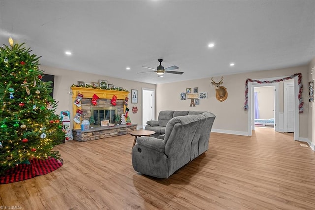 living room with light hardwood / wood-style flooring, ceiling fan, and a stone fireplace