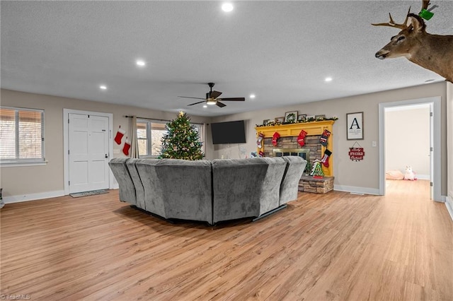 living room featuring ceiling fan, light hardwood / wood-style floors, a stone fireplace, and a textured ceiling