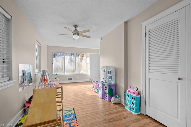 game room with a textured ceiling, light wood-type flooring, and ceiling fan