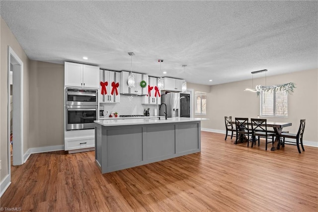 kitchen featuring a kitchen island with sink, light hardwood / wood-style flooring, appliances with stainless steel finishes, decorative light fixtures, and white cabinetry