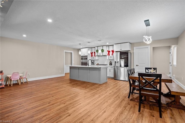 kitchen featuring appliances with stainless steel finishes, a kitchen island with sink, light hardwood / wood-style floors, white cabinetry, and hanging light fixtures