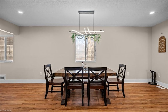 dining area with hardwood / wood-style flooring, plenty of natural light, a textured ceiling, and an inviting chandelier