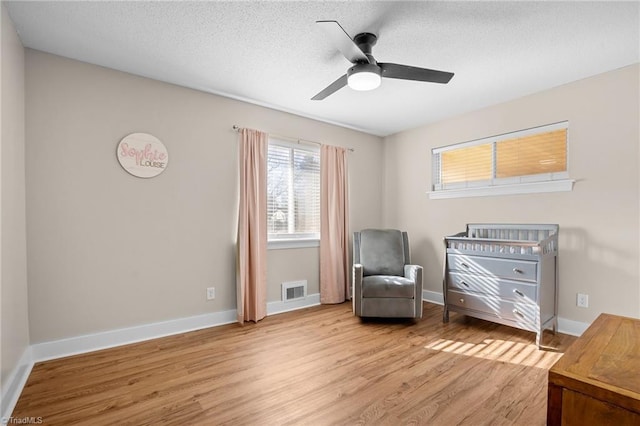 sitting room featuring ceiling fan, light hardwood / wood-style floors, and a textured ceiling