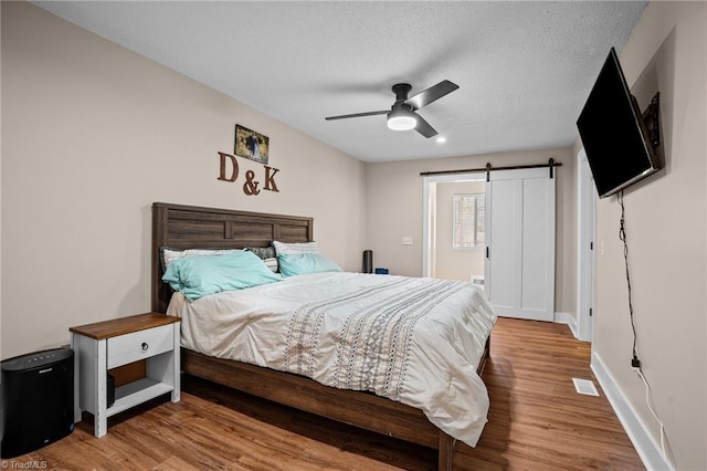 bedroom featuring a textured ceiling, a barn door, hardwood / wood-style flooring, and ceiling fan