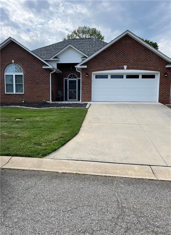 view of front of property featuring driveway, a front yard, brick siding, an attached garage, and a shingled roof