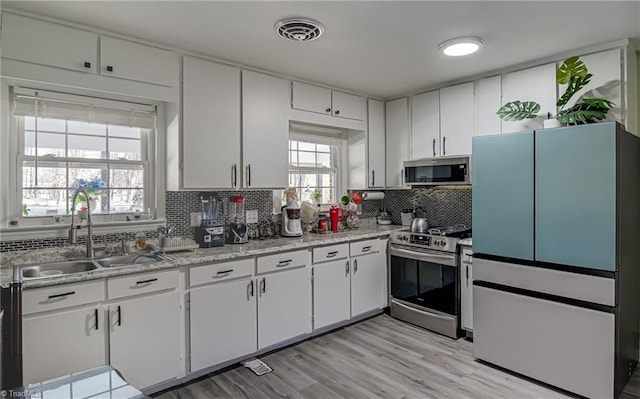 kitchen with appliances with stainless steel finishes, a sink, light countertops, white cabinetry, and tasteful backsplash