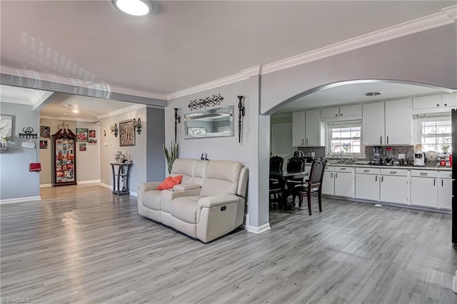 living area with arched walkways, ornamental molding, baseboards, and light wood finished floors