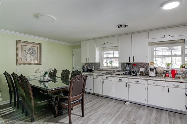 kitchen featuring decorative backsplash, ornamental molding, white cabinets, a sink, and light wood finished floors