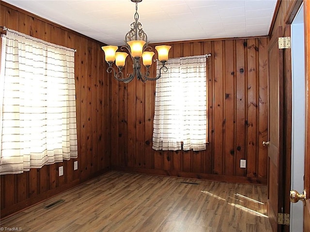 unfurnished dining area with wooden walls, a notable chandelier, wood finished floors, and visible vents