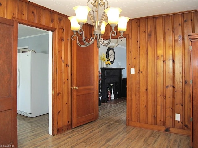 unfurnished dining area featuring wooden walls, ornamental molding, an inviting chandelier, and wood finished floors