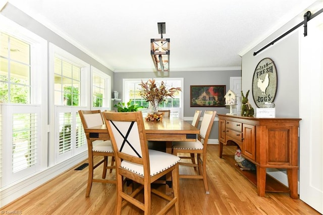 dining area featuring a barn door, light wood-type flooring, and ornamental molding