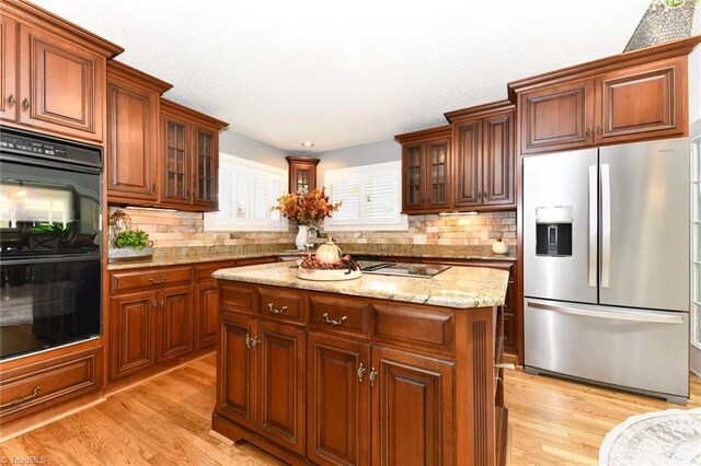 kitchen with backsplash, black appliances, a center island, light stone countertops, and light hardwood / wood-style floors