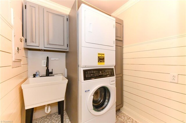 clothes washing area with cabinets, stacked washing maching and dryer, crown molding, and wooden walls