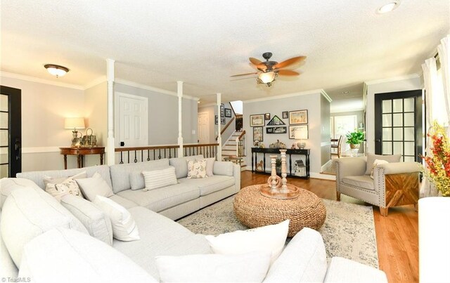 living room with a textured ceiling, ceiling fan, ornamental molding, and wood-type flooring