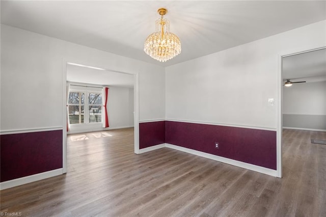 empty room with hardwood / wood-style flooring and ceiling fan with notable chandelier