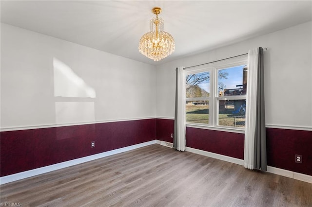 empty room with hardwood / wood-style floors and a chandelier