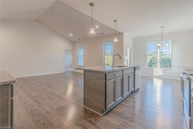 kitchen featuring dark hardwood / wood-style flooring, a kitchen island with sink, light stone counters, and decorative light fixtures