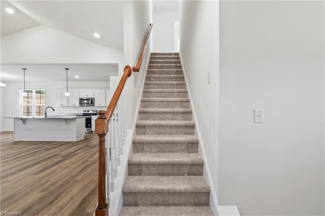 stairway with dark wood-type flooring, high vaulted ceiling, and sink