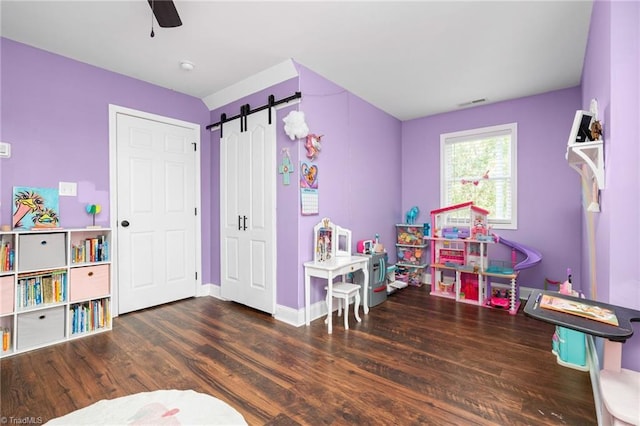 game room featuring dark wood-type flooring, ceiling fan, and a barn door