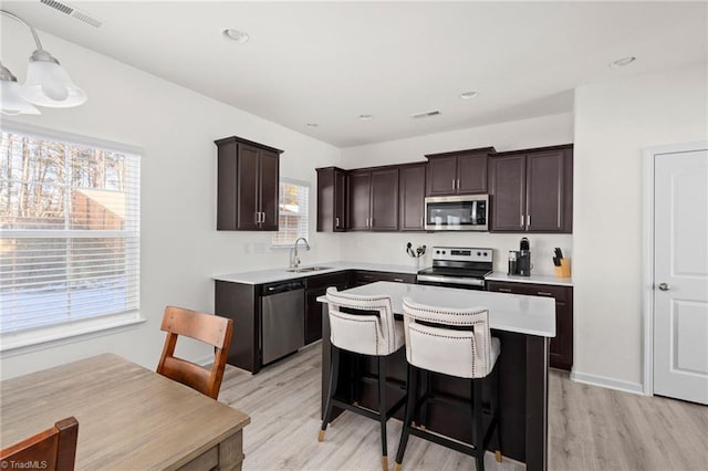 kitchen with appliances with stainless steel finishes, sink, a center island, light hardwood / wood-style floors, and hanging light fixtures