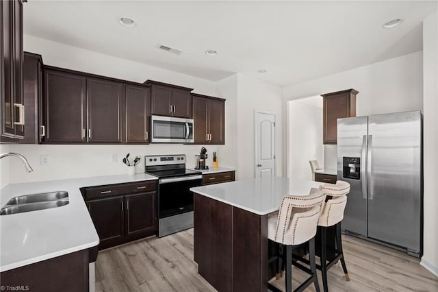 kitchen with a kitchen breakfast bar, sink, light hardwood / wood-style floors, a kitchen island, and stainless steel appliances