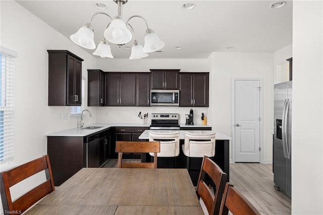 kitchen with sink, stainless steel appliances, an inviting chandelier, pendant lighting, and light wood-type flooring