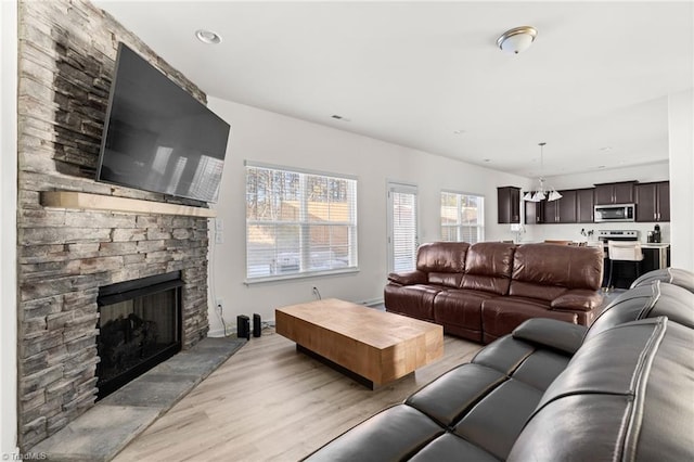 living room featuring an inviting chandelier, a stone fireplace, and light hardwood / wood-style flooring