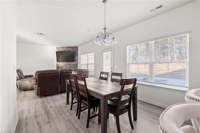 dining area featuring a fireplace, a chandelier, and light wood-type flooring