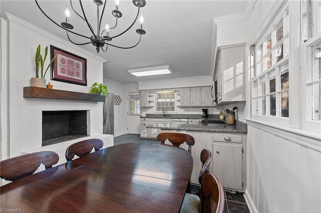 dining space with ornamental molding, a chandelier, sink, and a brick fireplace