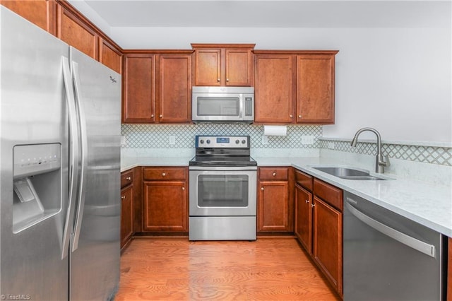 kitchen featuring sink, decorative backsplash, light stone countertops, light hardwood / wood-style floors, and stainless steel appliances