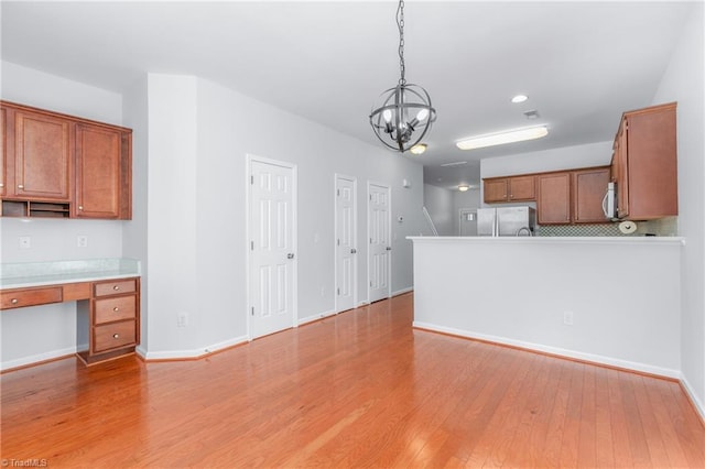 kitchen with an inviting chandelier, stainless steel refrigerator, hanging light fixtures, and light hardwood / wood-style floors