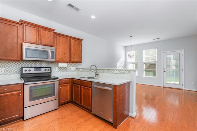 kitchen with hanging light fixtures, kitchen peninsula, sink, and appliances with stainless steel finishes