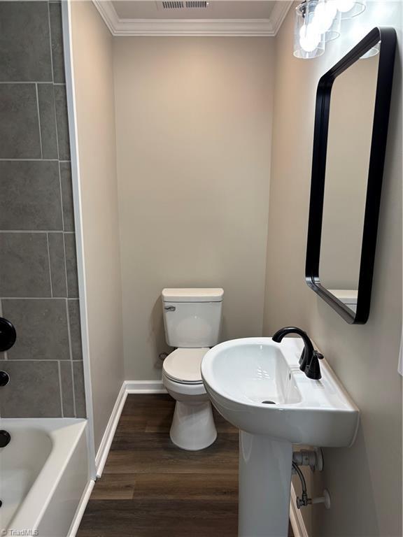 full bathroom with toilet, sink, crown molding, tiled shower / bath, and wood-type flooring