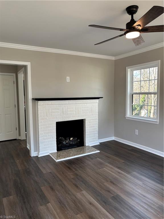 unfurnished living room featuring ornamental molding, dark wood-type flooring, ceiling fan, and a fireplace