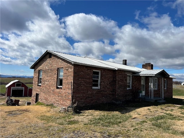 view of property exterior with an outbuilding, brick siding, a yard, a chimney, and metal roof