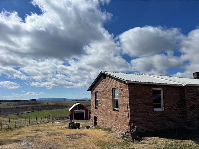 view of side of property featuring a storage shed, metal roof, fence, an outdoor structure, and brick siding