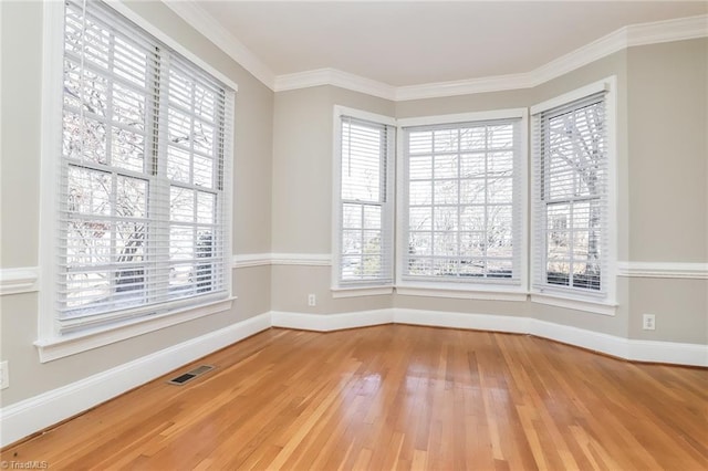 spare room with visible vents, light wood-style flooring, crown molding, and a healthy amount of sunlight