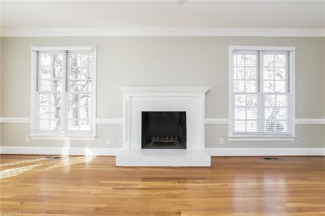 unfurnished living room with crown molding, a brick fireplace, plenty of natural light, and wood finished floors