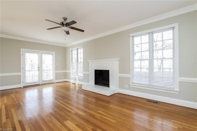 unfurnished living room with wood finished floors, visible vents, baseboards, a fireplace with raised hearth, and crown molding