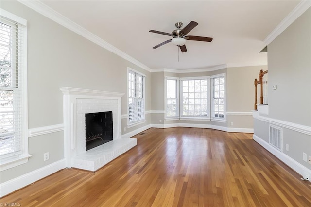 unfurnished living room with visible vents, a brick fireplace, baseboards, ornamental molding, and wood finished floors