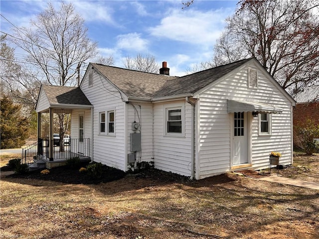 back of property featuring a shingled roof, a porch, and a chimney