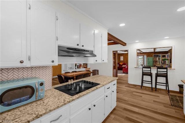 kitchen with decorative backsplash, black electric stovetop, light wood-type flooring, under cabinet range hood, and white cabinets