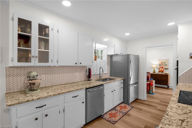 kitchen featuring white cabinetry, a sink, light wood-style flooring, backsplash, and stainless steel appliances