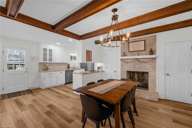 dining space with a brick fireplace, beamed ceiling, light wood-style floors, recessed lighting, and a chandelier
