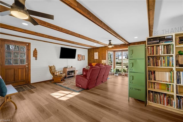 living area featuring wood finished floors, ceiling fan, beam ceiling, and wooden walls