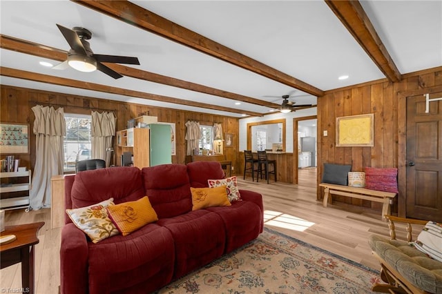 living area featuring ceiling fan, beamed ceiling, wood walls, and wood finished floors